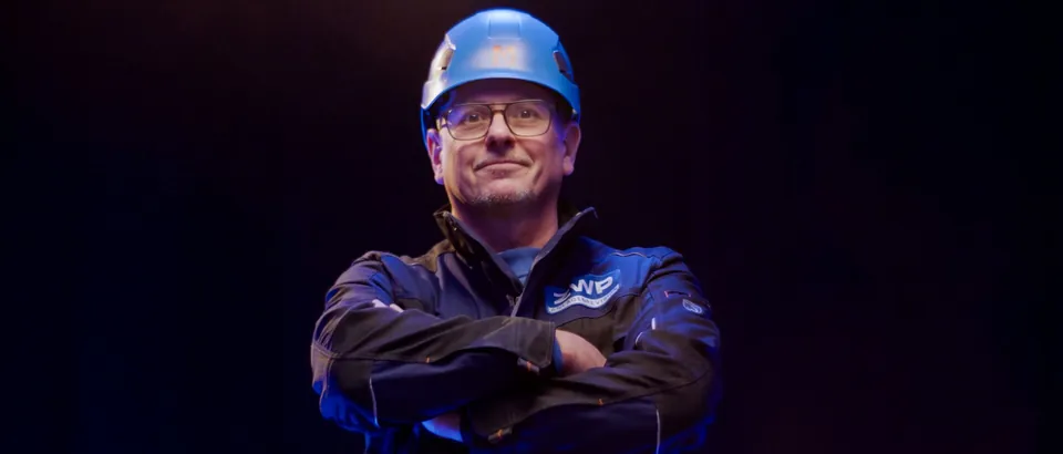 Mitarbeiter der ZWP mit blauem Schutzhelm und verschränkten Armen vor dunklem Hintergrund, Szene aus dem Erklärfilm