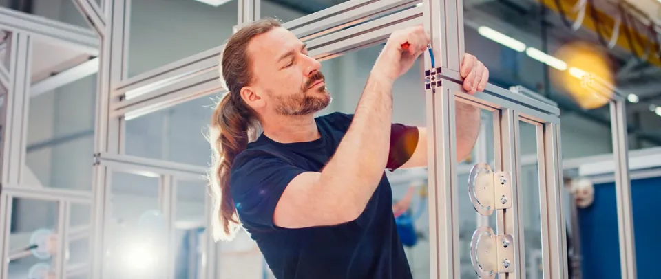 Mitarbeiter montiert ein Aluminium Profilsystem in der Halle von MiniTec, Szene aus dem Imagefilm